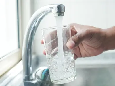 A hand holding a glass under a running kitchen faucet as clear water fills the glass.
