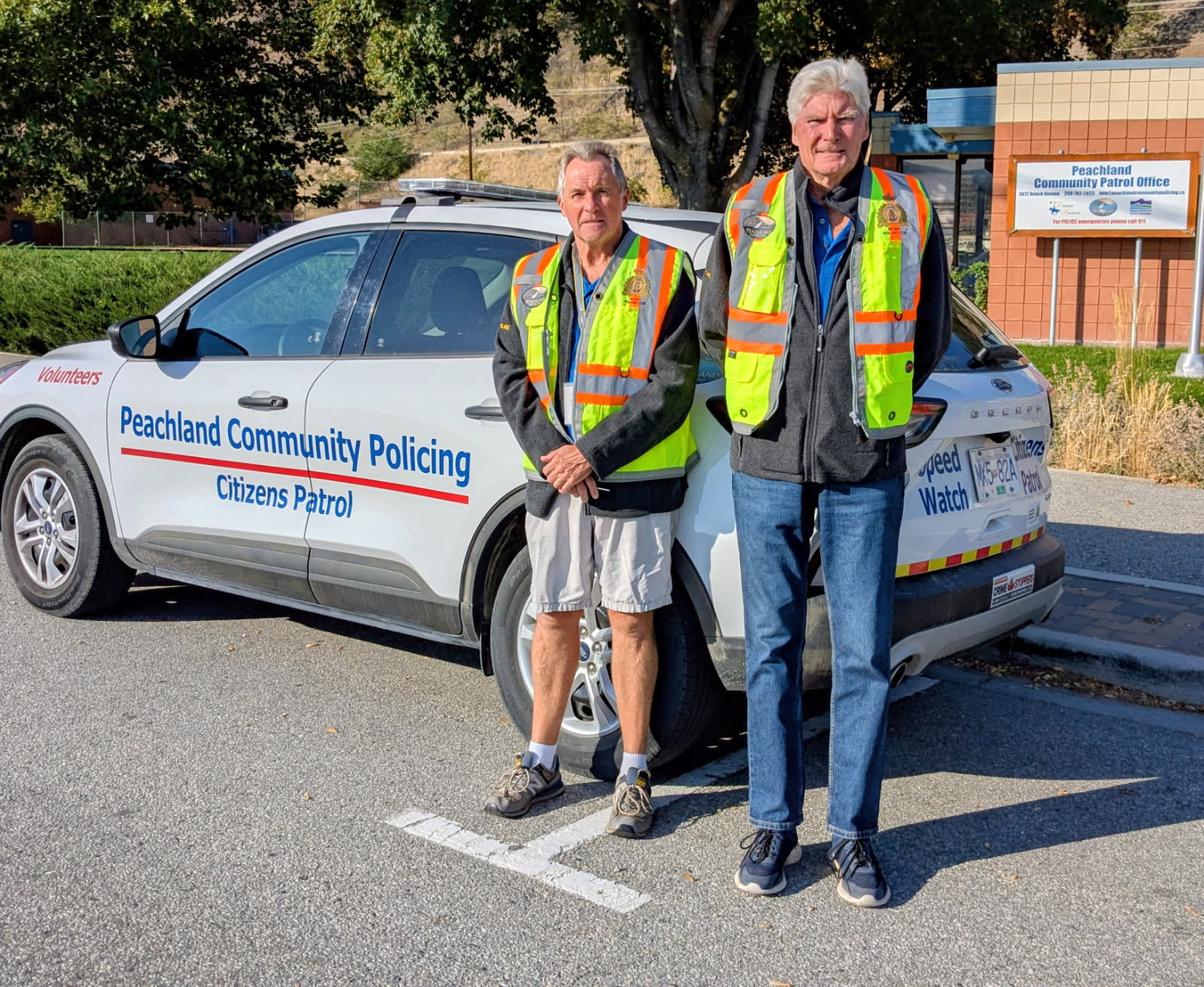 Two community policing volunteers stand beside a Peachland Community Policing Citizens Patrol vehicle.