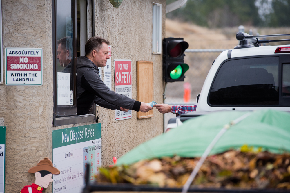 An attendant accepts payment from a driver at a scale house as a vehicle with yard waste waits.