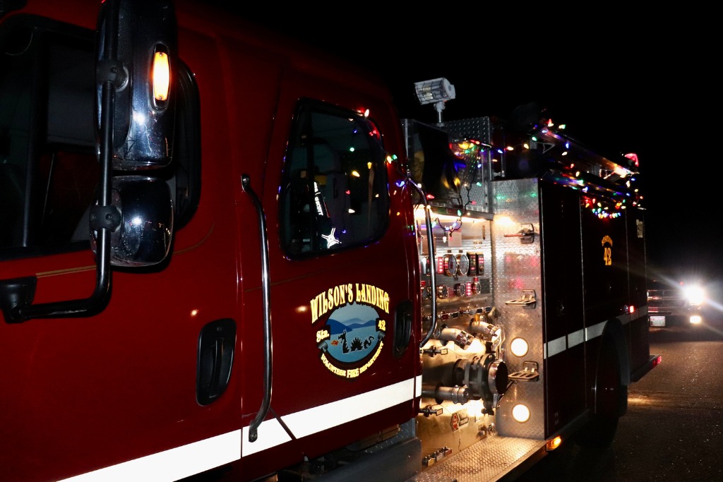 Red fire truck decorated with holiday lights parked on a dark road.